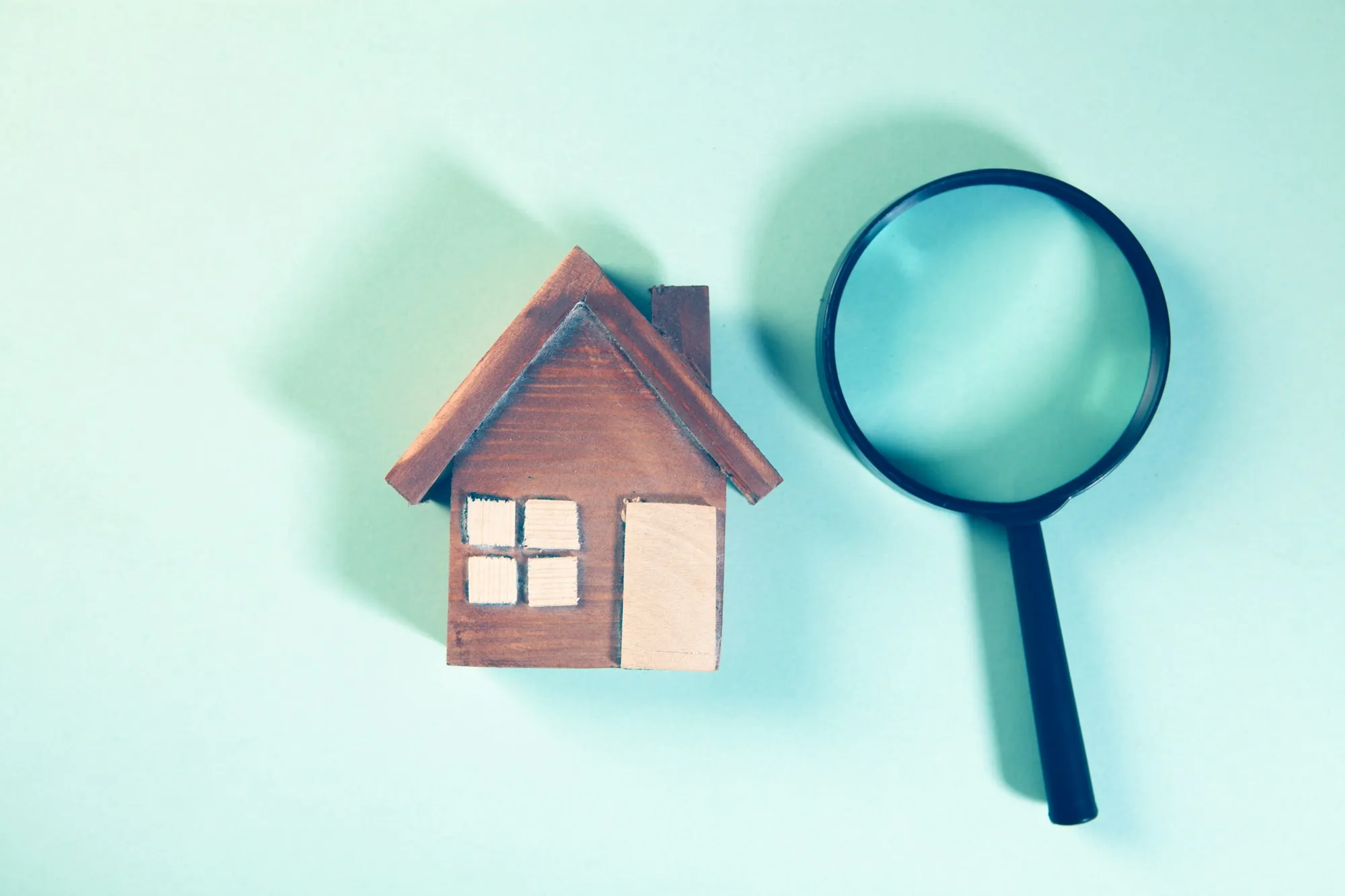 Wooden model house next to a magnifying glass